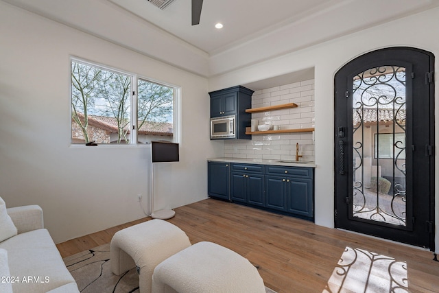 interior space with light hardwood / wood-style floors, stainless steel microwave, blue cabinetry, and tasteful backsplash