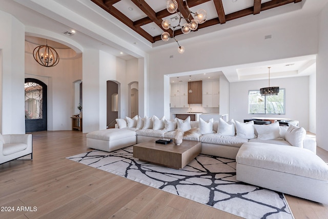 living room featuring beam ceiling, light hardwood / wood-style flooring, a high ceiling, and a notable chandelier