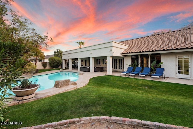 pool at dusk with an outdoor hangout area, a patio, and a lawn