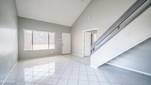 entrance foyer featuring high vaulted ceiling, light tile patterned flooring, baseboards, and stairs