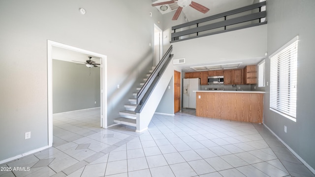 kitchen with light tile patterned floors, white refrigerator with ice dispenser, brown cabinetry, a towering ceiling, and stainless steel microwave