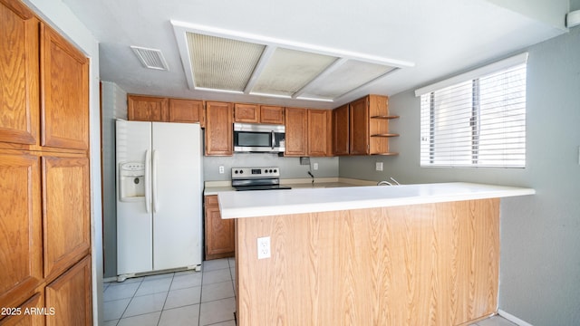 kitchen featuring light tile patterned flooring, a peninsula, visible vents, appliances with stainless steel finishes, and brown cabinetry