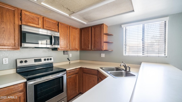 kitchen with brown cabinets, stainless steel appliances, light countertops, open shelves, and a sink