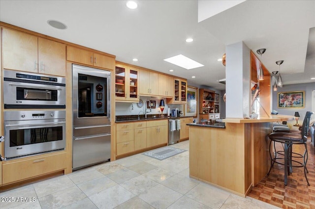 kitchen with appliances with stainless steel finishes, light brown cabinetry, a skylight, a kitchen breakfast bar, and kitchen peninsula