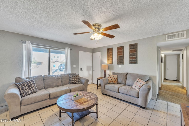 living room with visible vents, a textured wall, light tile patterned flooring, a textured ceiling, and a ceiling fan