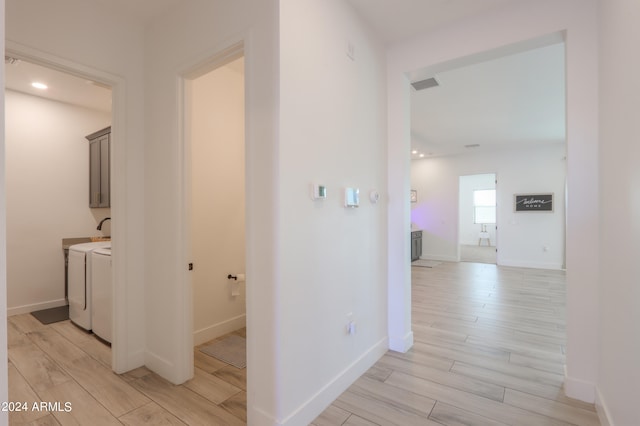 hallway with light hardwood / wood-style floors and separate washer and dryer