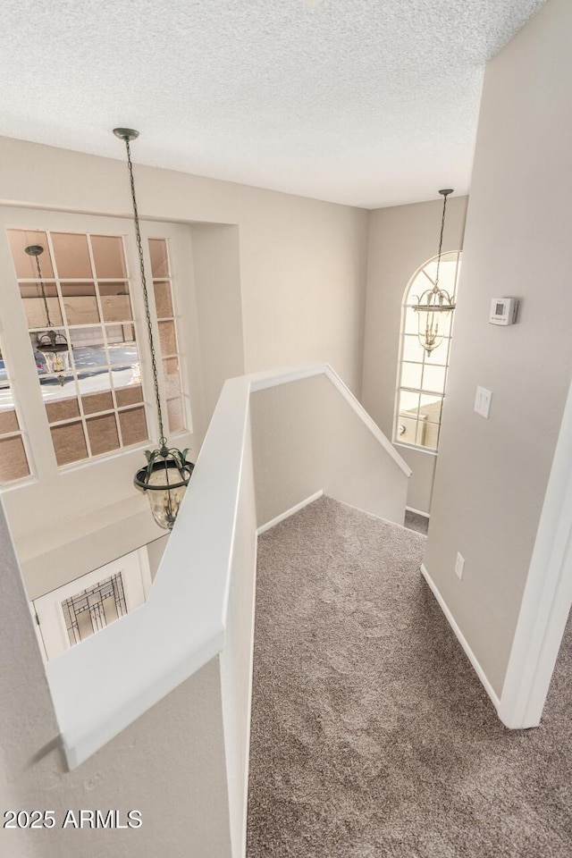 hallway featuring an upstairs landing, carpet, a textured ceiling, and baseboards