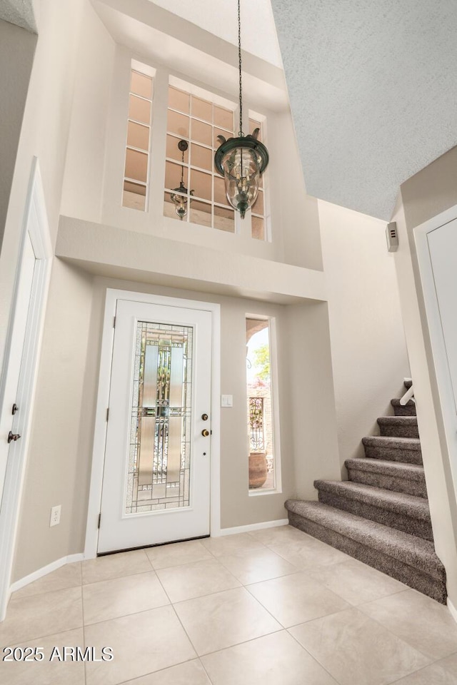 entrance foyer featuring high vaulted ceiling, stairs, a chandelier, tile patterned floors, and baseboards