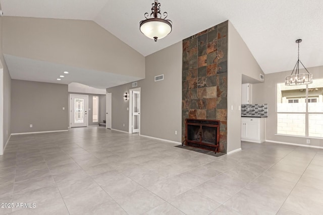 unfurnished living room with light tile patterned flooring, a chandelier, high vaulted ceiling, a fireplace, and baseboards