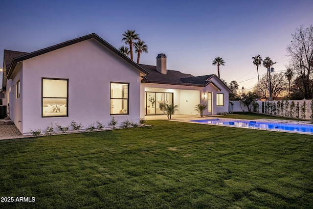 back house at dusk with a patio area, a fenced in pool, and a lawn