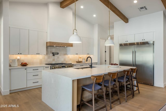 kitchen with beamed ceiling, white cabinetry, built in fridge, and sink