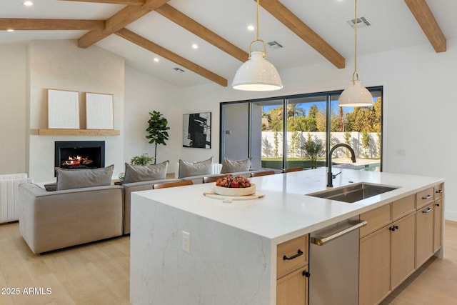 kitchen featuring a center island with sink, lofted ceiling with beams, a large fireplace, sink, and light brown cabinets