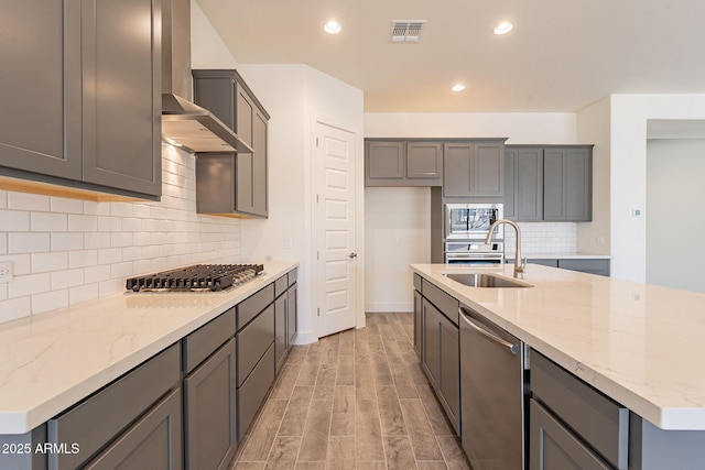 kitchen featuring gray cabinets, appliances with stainless steel finishes, sink, light wood-type flooring, and wall chimney exhaust hood