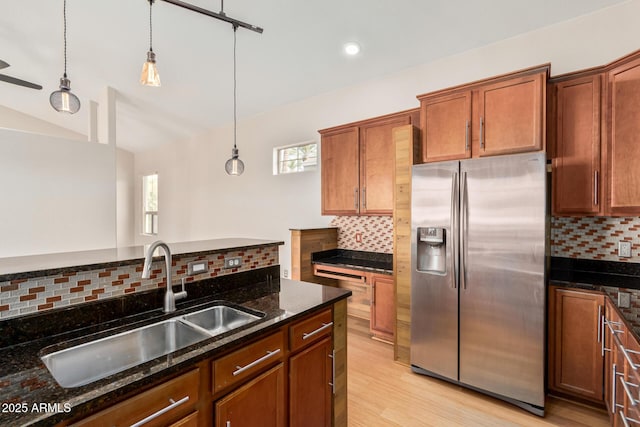 kitchen featuring lofted ceiling, a sink, stainless steel refrigerator with ice dispenser, dark stone counters, and decorative light fixtures