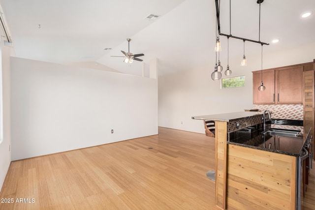 kitchen with visible vents, lofted ceiling, a sink, light wood-type flooring, and backsplash