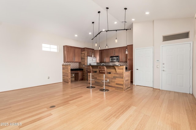 kitchen featuring light wood finished floors, a high ceiling, decorative backsplash, appliances with stainless steel finishes, and a kitchen bar