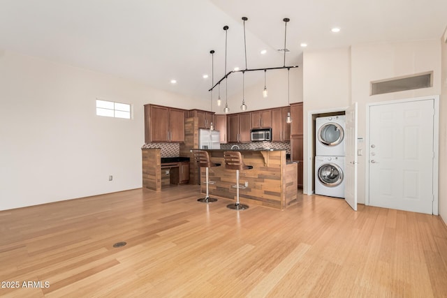 kitchen featuring decorative backsplash, stacked washer / dryer, light wood-style flooring, a breakfast bar, and stainless steel appliances