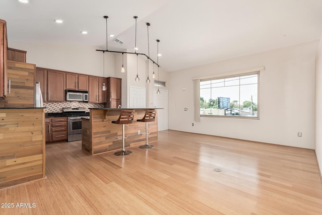 kitchen with a kitchen breakfast bar, appliances with stainless steel finishes, backsplash, brown cabinets, and dark countertops