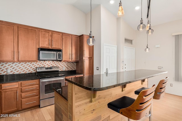 kitchen featuring decorative backsplash, appliances with stainless steel finishes, brown cabinets, dark stone countertops, and a kitchen bar