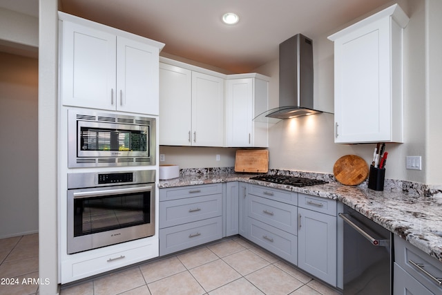 kitchen featuring gray cabinetry, white cabinets, wall chimney range hood, and stainless steel appliances