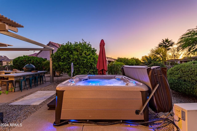 patio terrace at dusk featuring a hot tub, an outdoor bar, and a grill