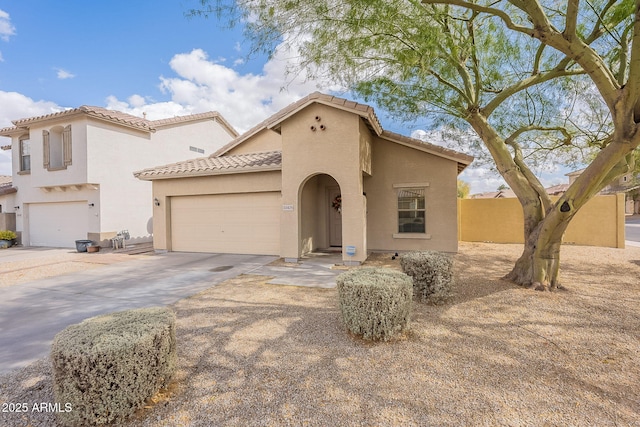 mediterranean / spanish-style house featuring a garage, fence, concrete driveway, a tiled roof, and stucco siding