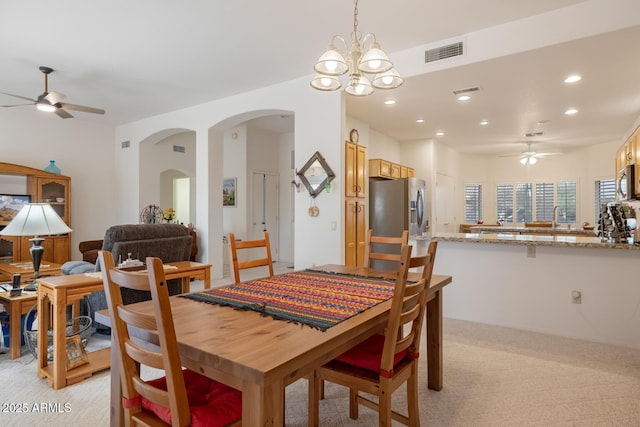 dining space with light colored carpet, sink, and ceiling fan with notable chandelier