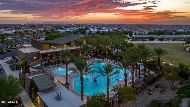 pool at dusk featuring a community pool, a patio area, and a residential view