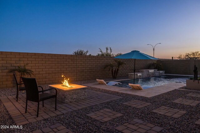 patio terrace at dusk with a fenced in pool, a fire pit, and a fenced backyard