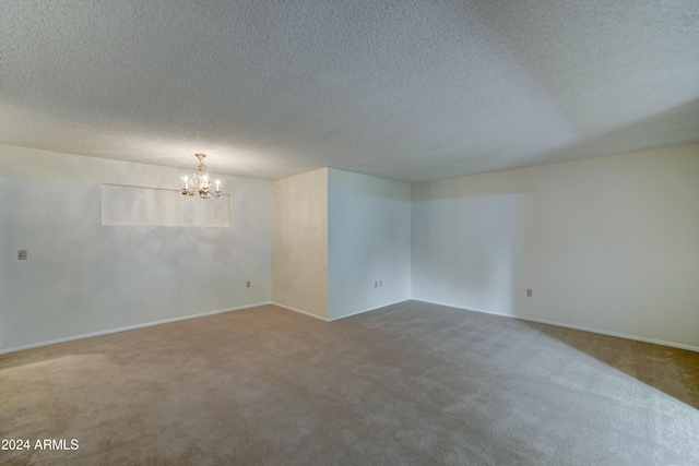 carpeted empty room with a textured ceiling and an inviting chandelier