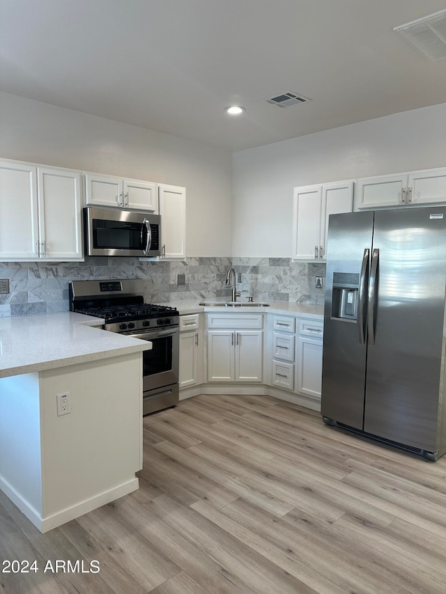 kitchen with appliances with stainless steel finishes, decorative backsplash, light wood-type flooring, and white cabinets