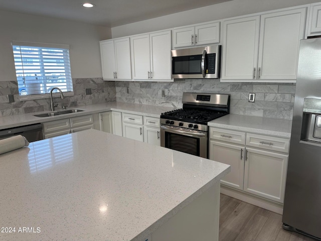 kitchen featuring appliances with stainless steel finishes, backsplash, sink, light wood-type flooring, and white cabinets