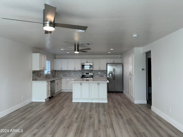 kitchen with appliances with stainless steel finishes, light hardwood / wood-style flooring, white cabinets, a center island, and ceiling fan