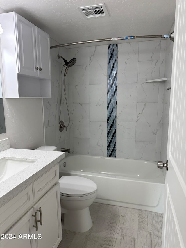 full bathroom with a textured ceiling, toilet, tiled shower / bath, and vanity