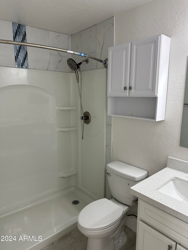 bathroom featuring toilet, vanity, tile patterned floors, tiled shower, and a textured ceiling