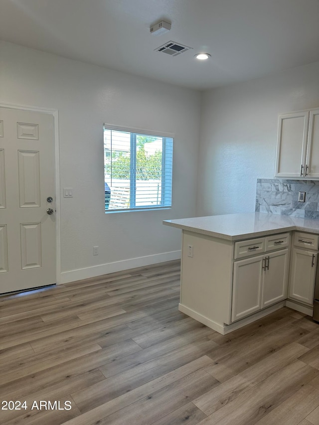 kitchen featuring kitchen peninsula, light hardwood / wood-style flooring, white cabinets, and tasteful backsplash