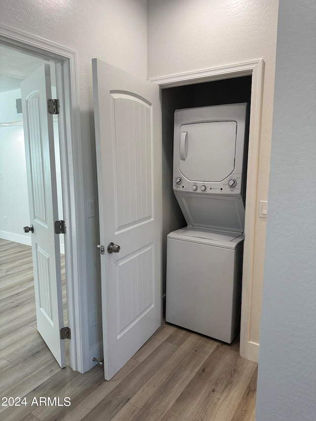 laundry room with light wood-type flooring and stacked washer / dryer