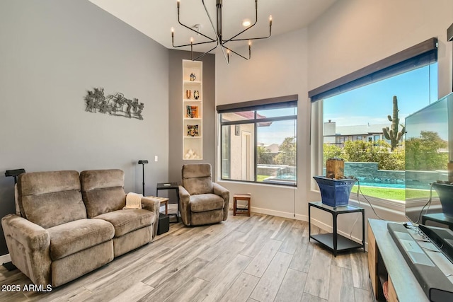 living room with a towering ceiling, a chandelier, and light hardwood / wood-style flooring