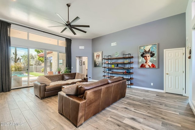 living room with a high ceiling, ceiling fan, and light wood-type flooring