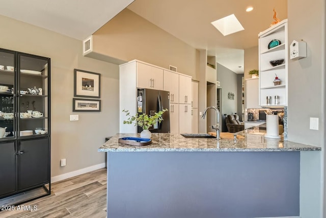 kitchen featuring sink, white cabinetry, stainless steel fridge with ice dispenser, kitchen peninsula, and light stone countertops