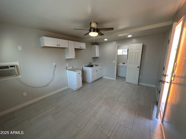 kitchen featuring a ceiling fan, a wall mounted air conditioner, a sink, baseboards, and light wood-style floors