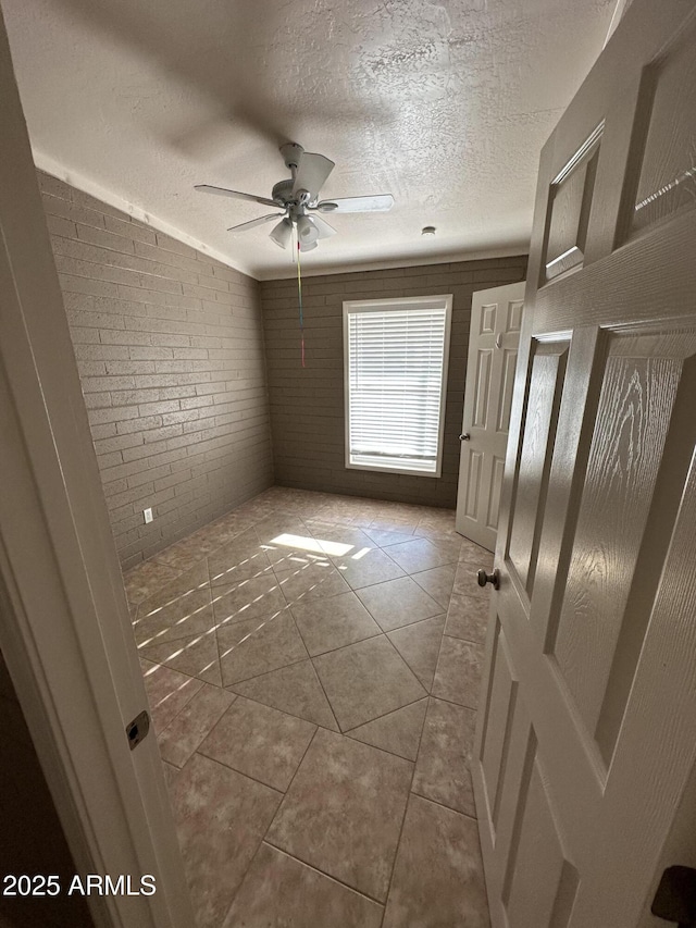 unfurnished room with brick wall, ceiling fan, a textured ceiling, and tile patterned flooring