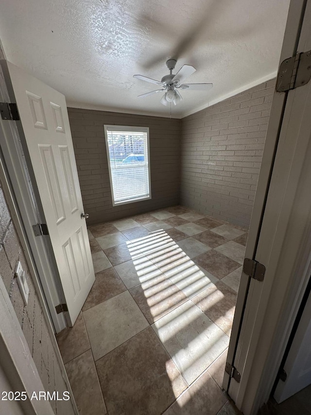 empty room with brick wall, a ceiling fan, and a textured ceiling