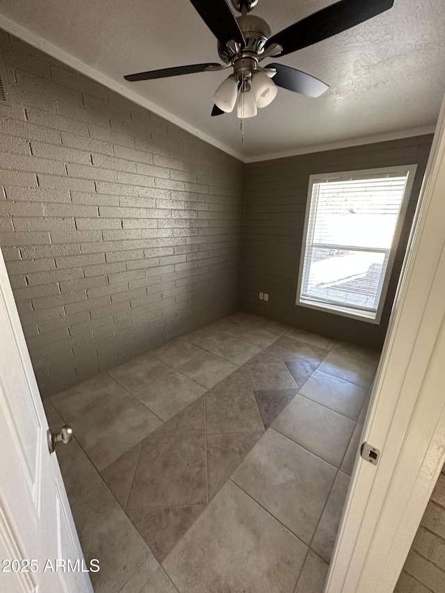 tiled spare room with brick wall, a ceiling fan, and ornamental molding
