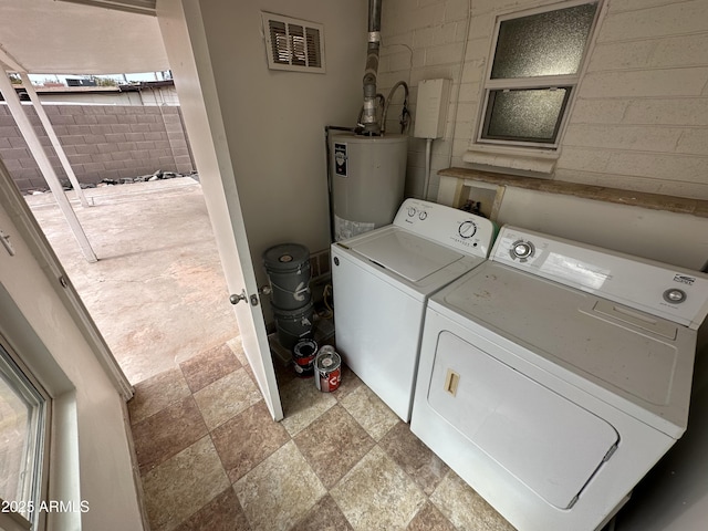 clothes washing area with independent washer and dryer, water heater, and light stone finish floors