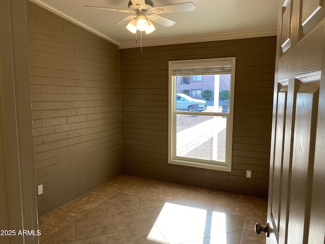 empty room with ornamental molding, tile patterned flooring, ceiling fan, and brick wall