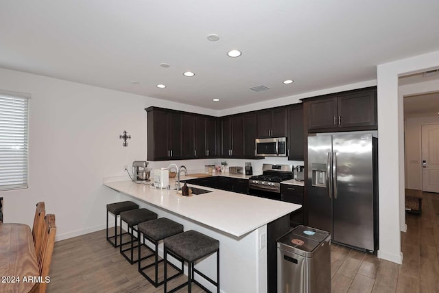 kitchen with sink, light hardwood / wood-style flooring, kitchen peninsula, a breakfast bar area, and appliances with stainless steel finishes