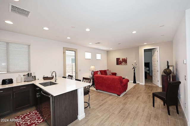 kitchen featuring dishwasher, a breakfast bar area, kitchen peninsula, sink, and light hardwood / wood-style flooring