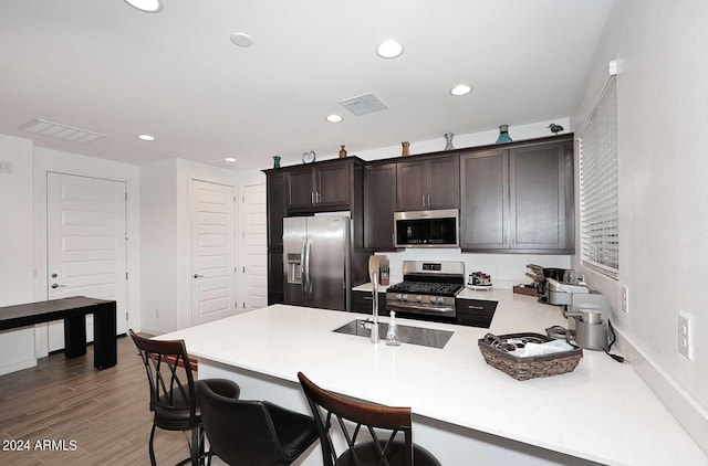 kitchen with stainless steel appliances, sink, a kitchen breakfast bar, dark brown cabinets, and dark wood-type flooring