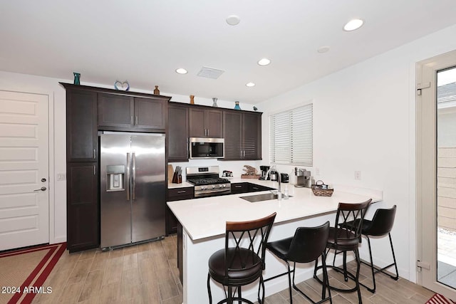 kitchen featuring sink, a kitchen breakfast bar, kitchen peninsula, dark brown cabinetry, and appliances with stainless steel finishes